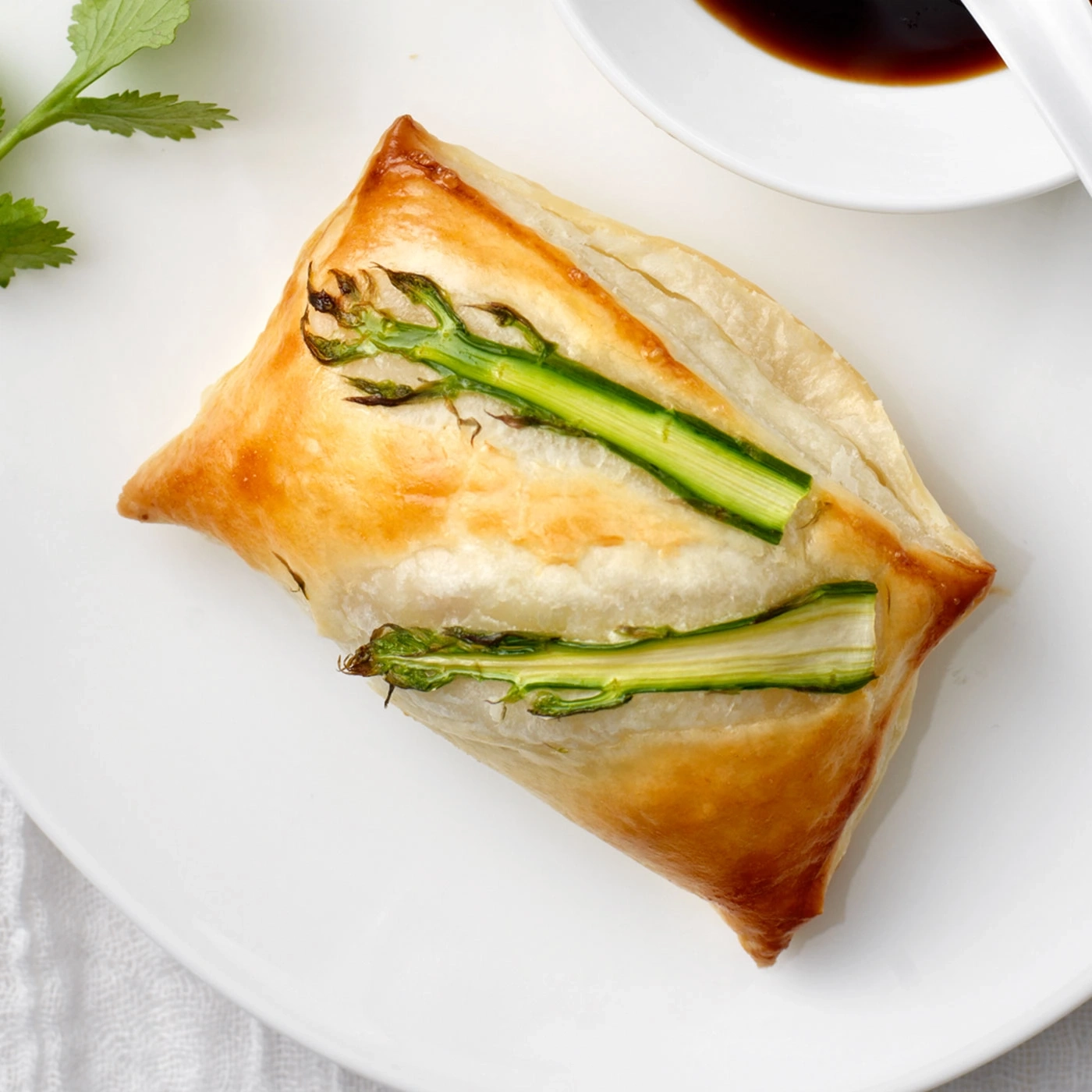 Pâtisserie avec asperges sur une assiette, sauce et herbes à côté.