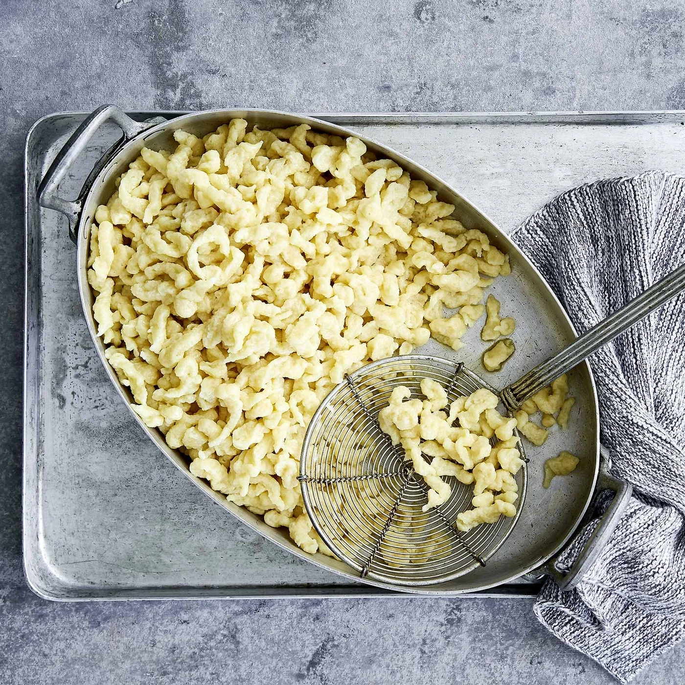 Spätzle in einer Schüssel mit einem Sieb und einem Tuch auf einem Tablett