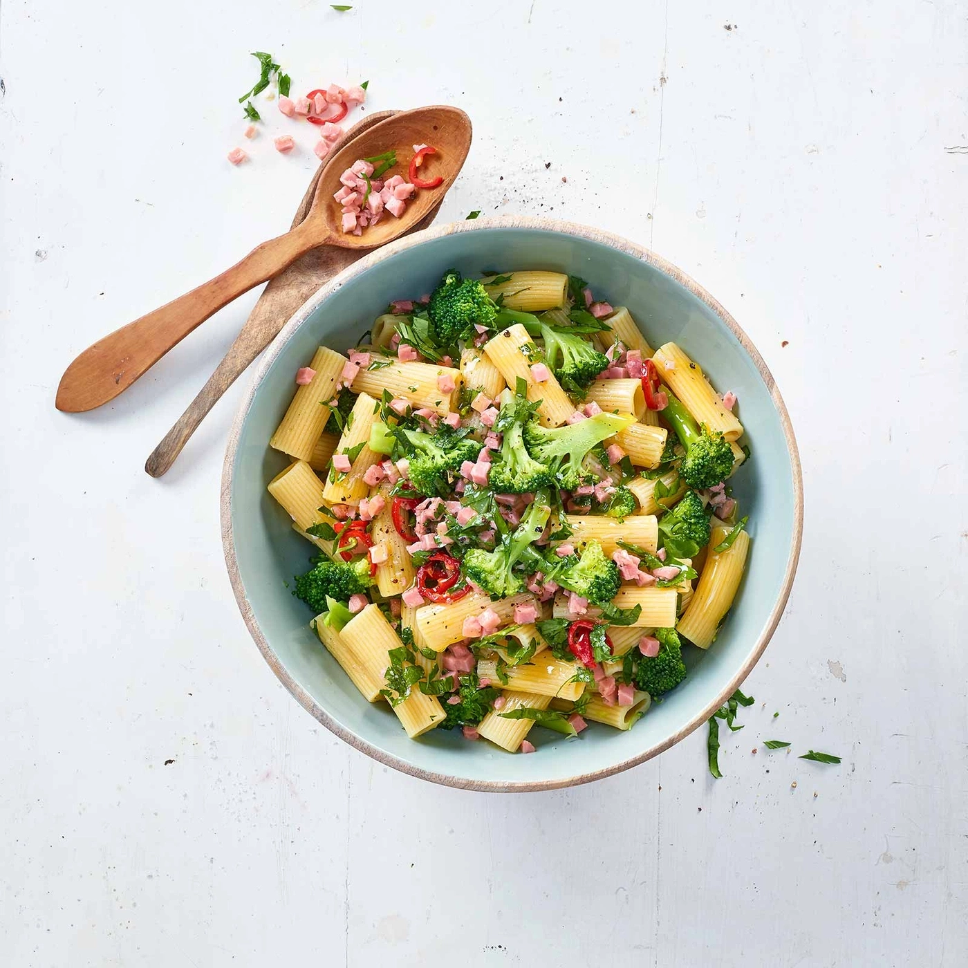 Pasta mit Brokkoli, Schinken und Kräutern in einer blauen Schüssel auf weißem Tisch
