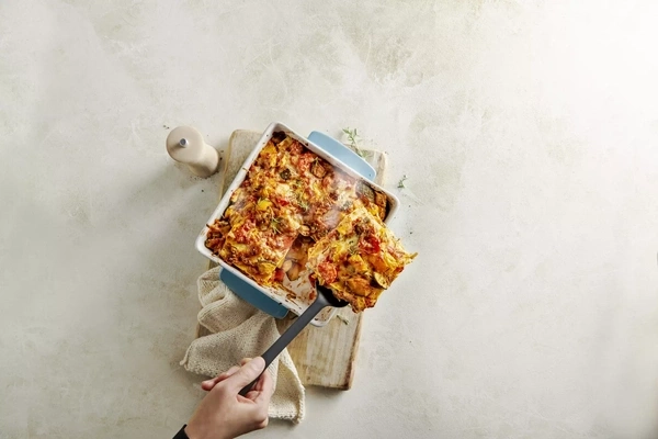 Auflaufform mit Lasagne wird mit einem Spatel herausgenommen.