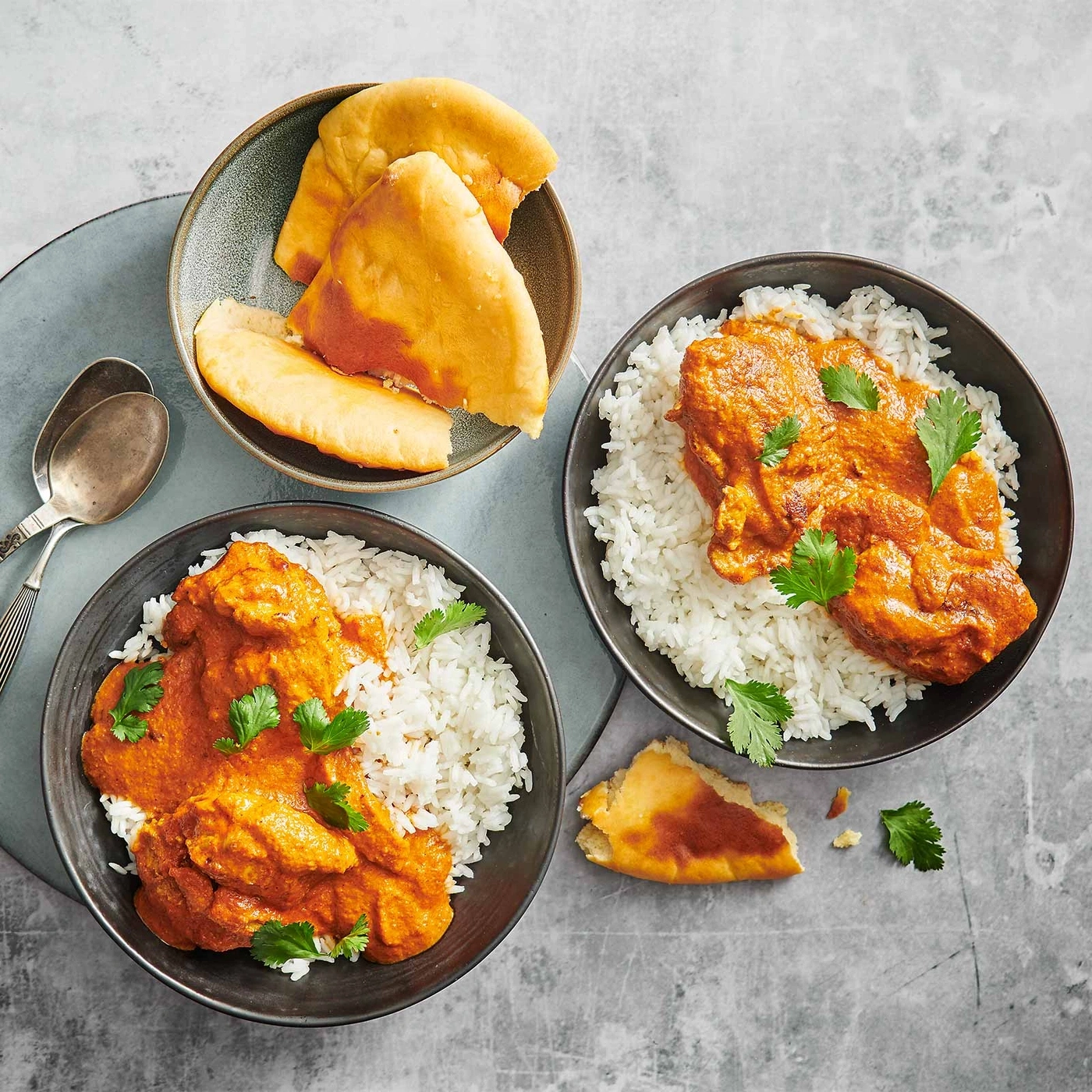 Indisches Essen mit Reis, Curry und Brot, serviert auf einem grauen Tisch.