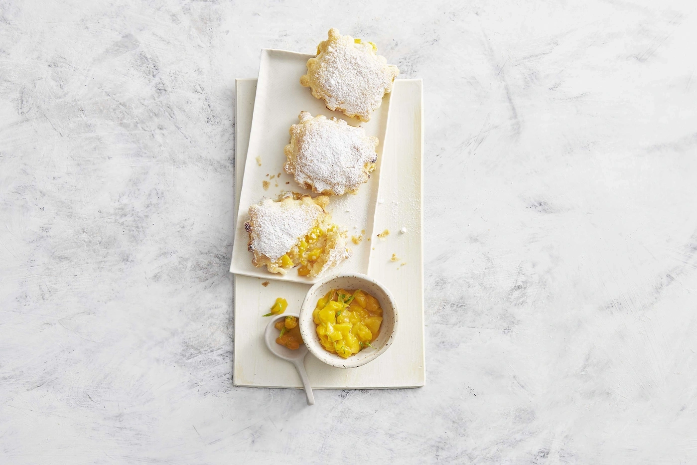 Drei Gebäckstücke mit Puderzucker auf einem Tablett mit Mango-Chutney.