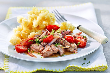 Teller mit Fleisch, Tomaten und Kartoffelpüree, serviert mit einer Gabel.