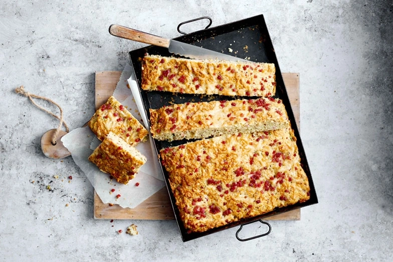 Käsekuchen mit Speck auf einem Tablett und Holzbrett mit Messer
