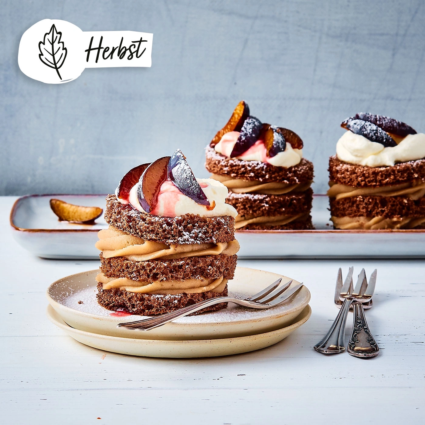 Kuchen mit Pflaumen, Sahne und Puderzucker auf Tellern mit Gabeln