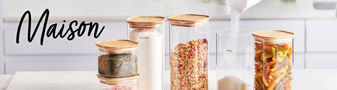 Des bocaux remplis d'aliments, dont de la farine, du granola, du sucre et des pâtes, sur une surface blanche.