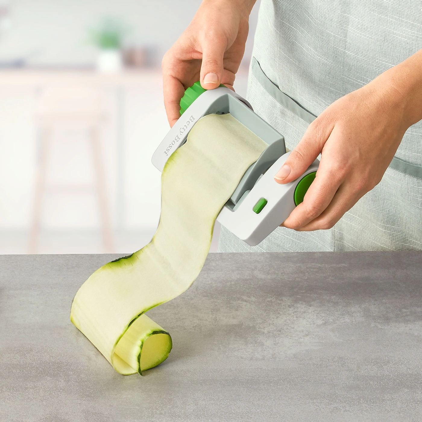 Person schneidet Zucchini mit einem Spiralschneider auf einer grauen Oberfläche.