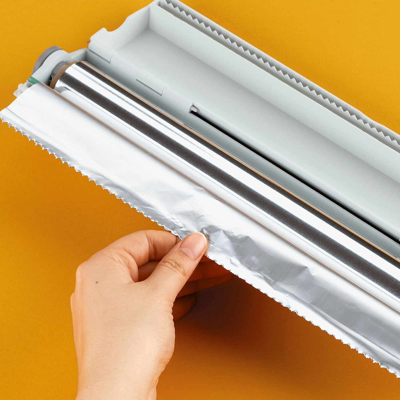 Papier d'aluminium tiré d'une boîte distributrice, fond jaune, gros plan de la main