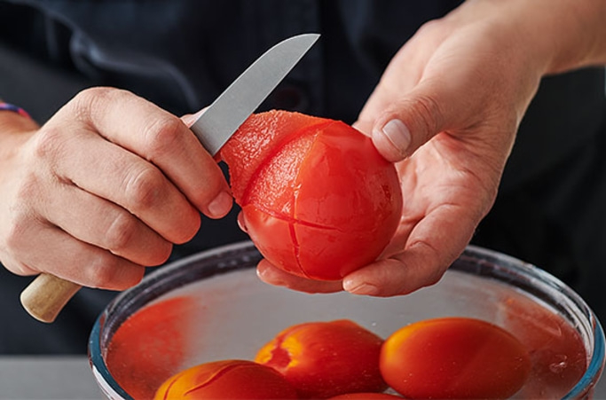 Person schält Tomate mit Messer. Tomaten in Schüssel. Nahaufnahme der Hände.