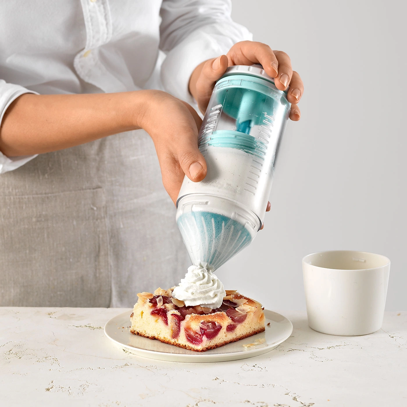 Person, die Sahne auf Kuchen mit Kirschen gibt, mit Becher.