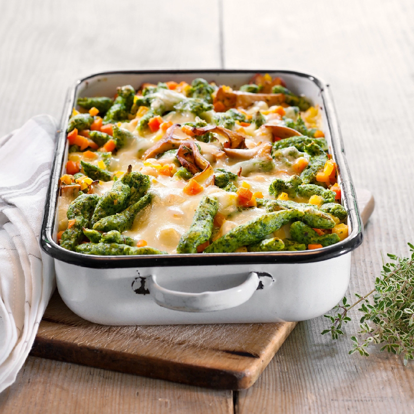 Gratin de spaetzle aux épinards, légumes et fromage dans un plat blanc