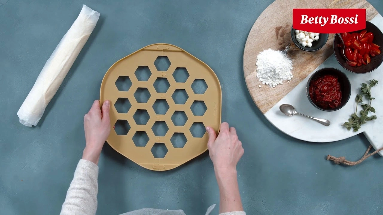 Personne tient moule à pâte, ingrédients sur planche, logo Betty Bossi, fond bleu.