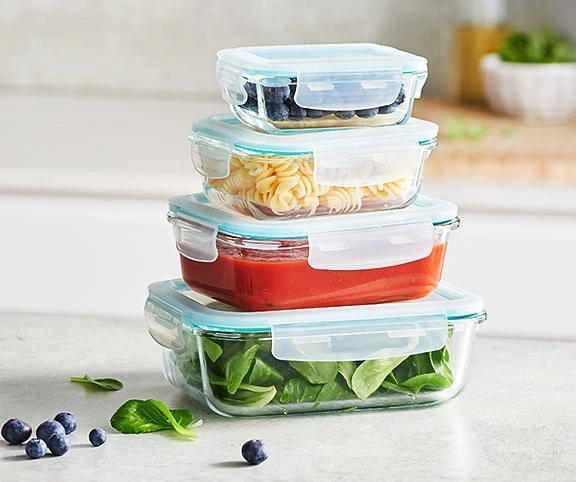 Quatre récipients en verre empilés avec aliments: myrtilles, pâtes, sauce, salade.