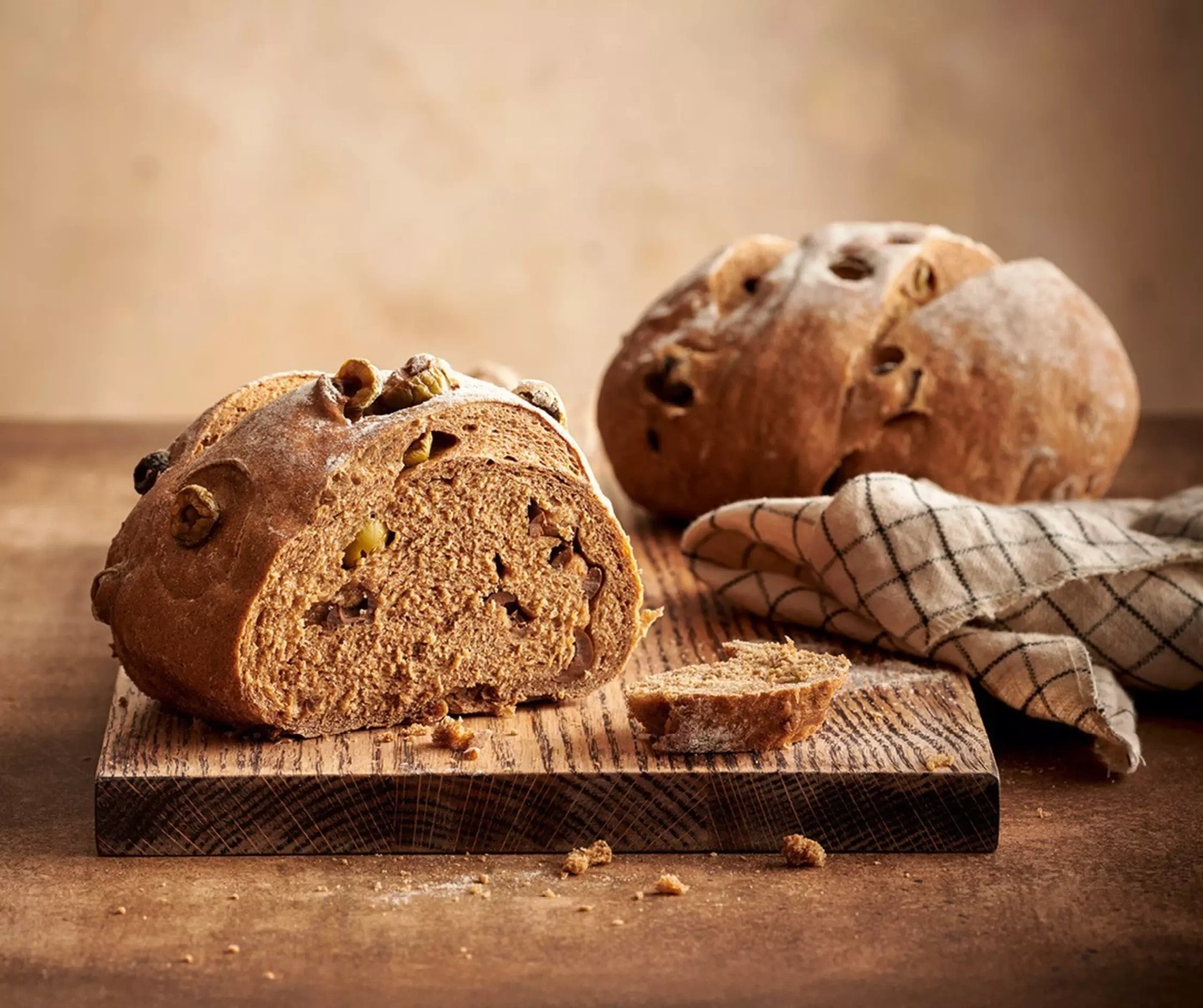 Un pain coupé avec des noix et des raisins sur une planche en bois.