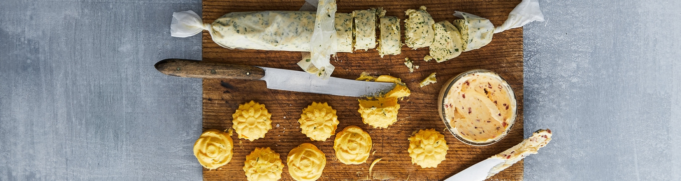 Holzbrett mit Kräuterbutter, Messer und Butterblumen-Keksen