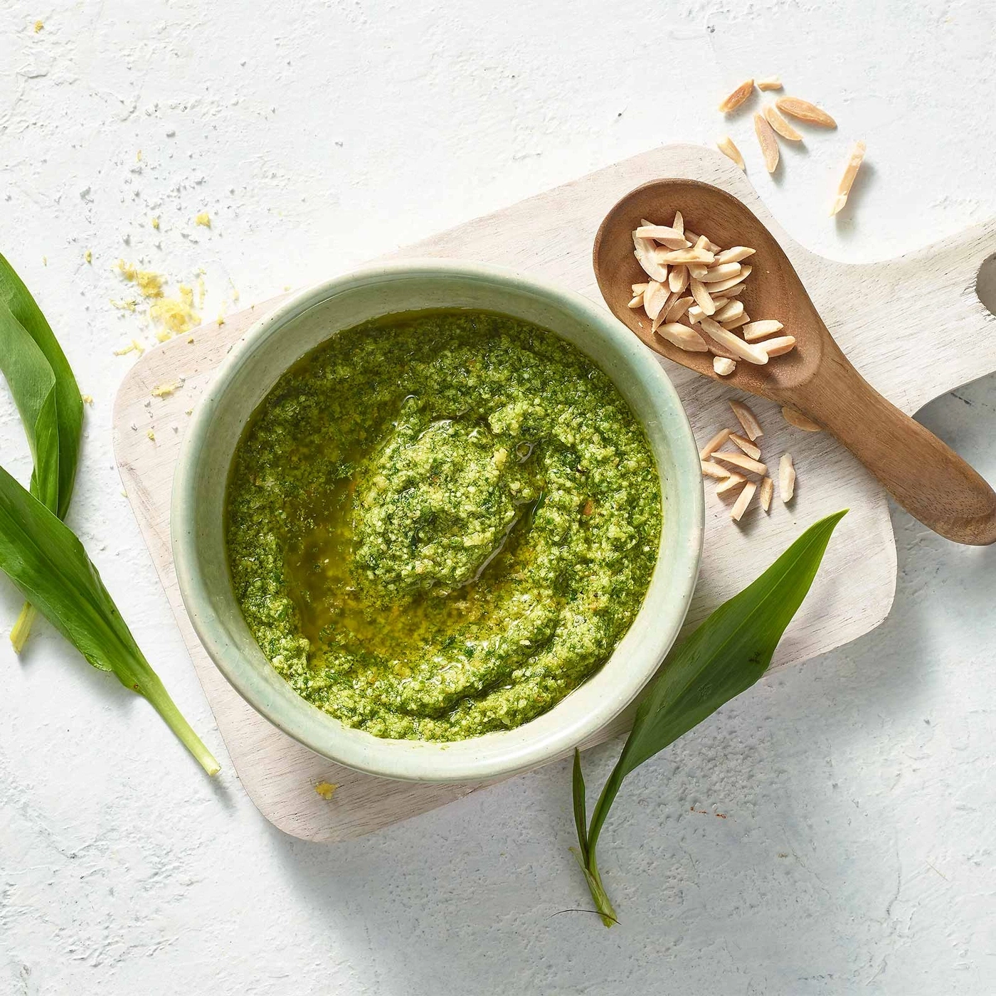 Grünes Pesto in einer Schüssel mit Mandeln und Blättern auf einem Brett
