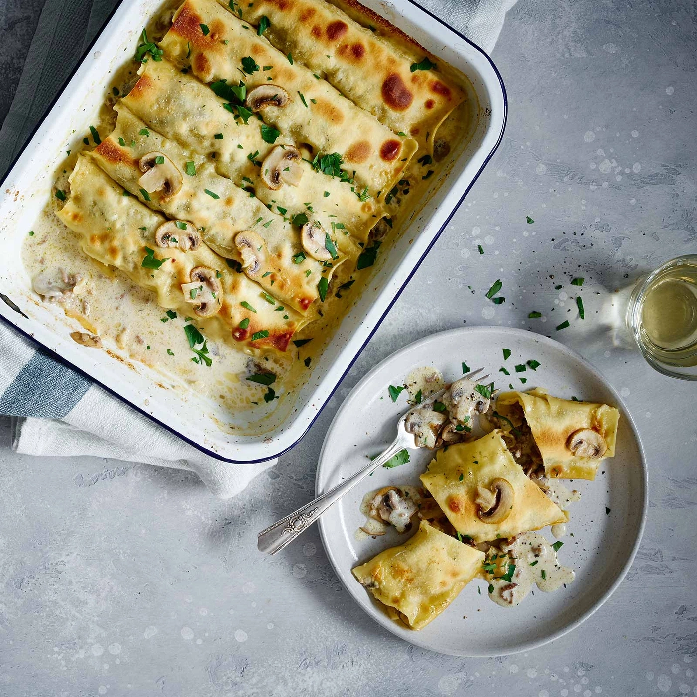 Cannelloni mit Pilzen und Sauce auf einem Teller und in einer Auflaufform