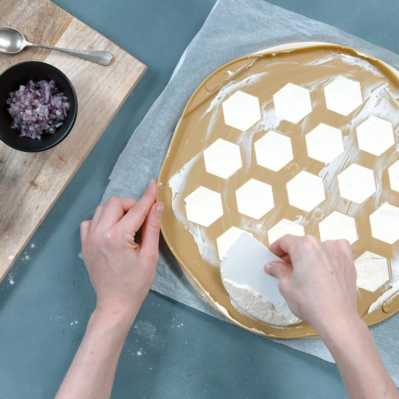 Mains étalant la pâte avec une spatule, oignons, sur un tapis de cuisson.