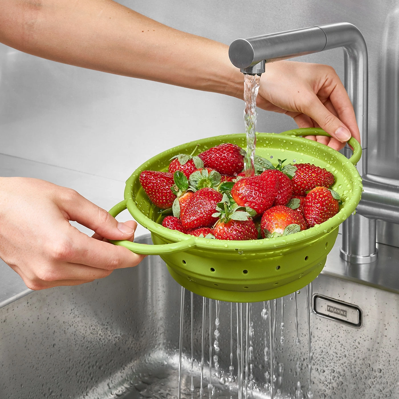 Erdbeeren werden in einem grünen Sieb unter fließendem Wasser gewaschen.