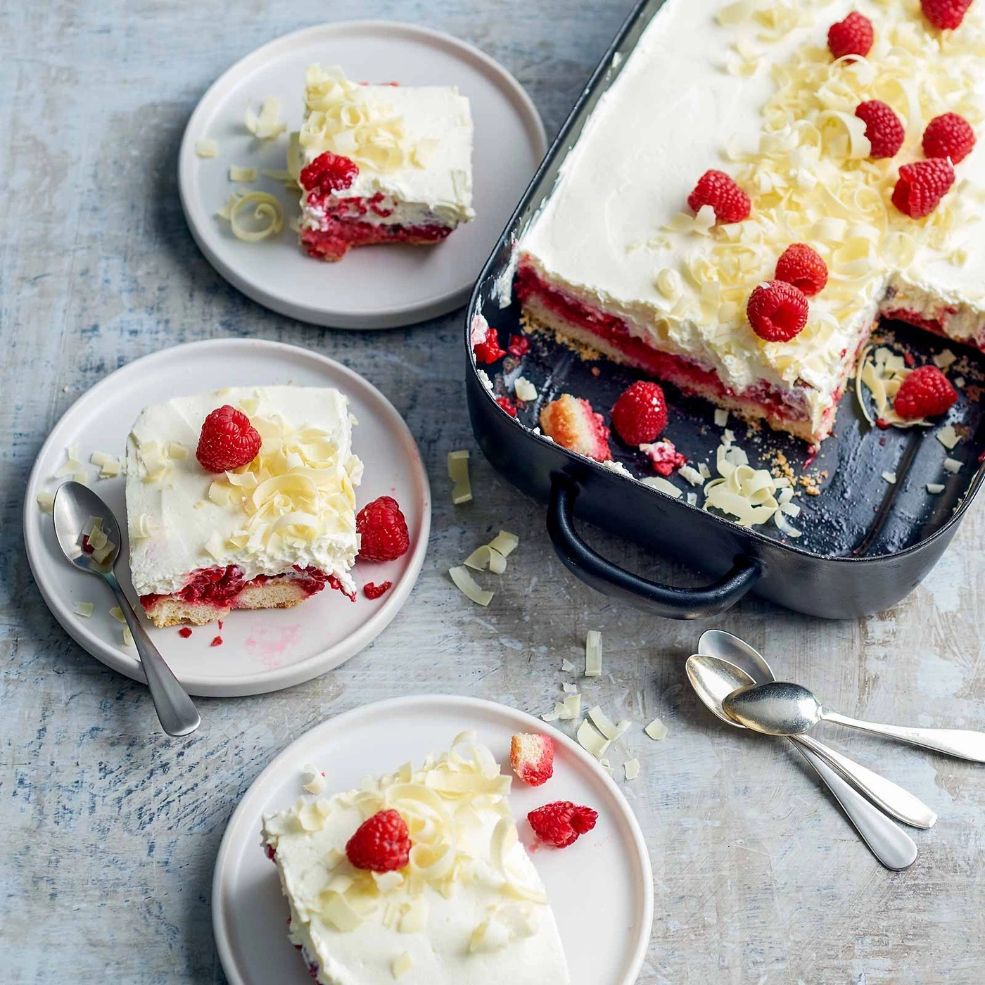 Himbeerkuchen mit Sahne, Schokolade und Beeren auf Tellern und in einer Form