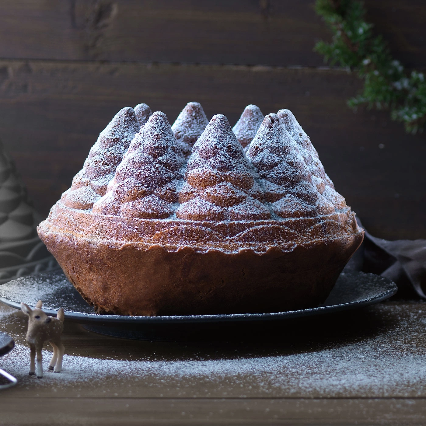Un gâteau en forme de sapin de Noël, saupoudré de sucre glace, sur une assiette.