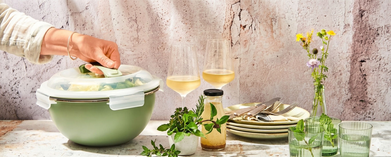 Grüne Schüssel mit Salat, Wein und Kräutern auf Tisch