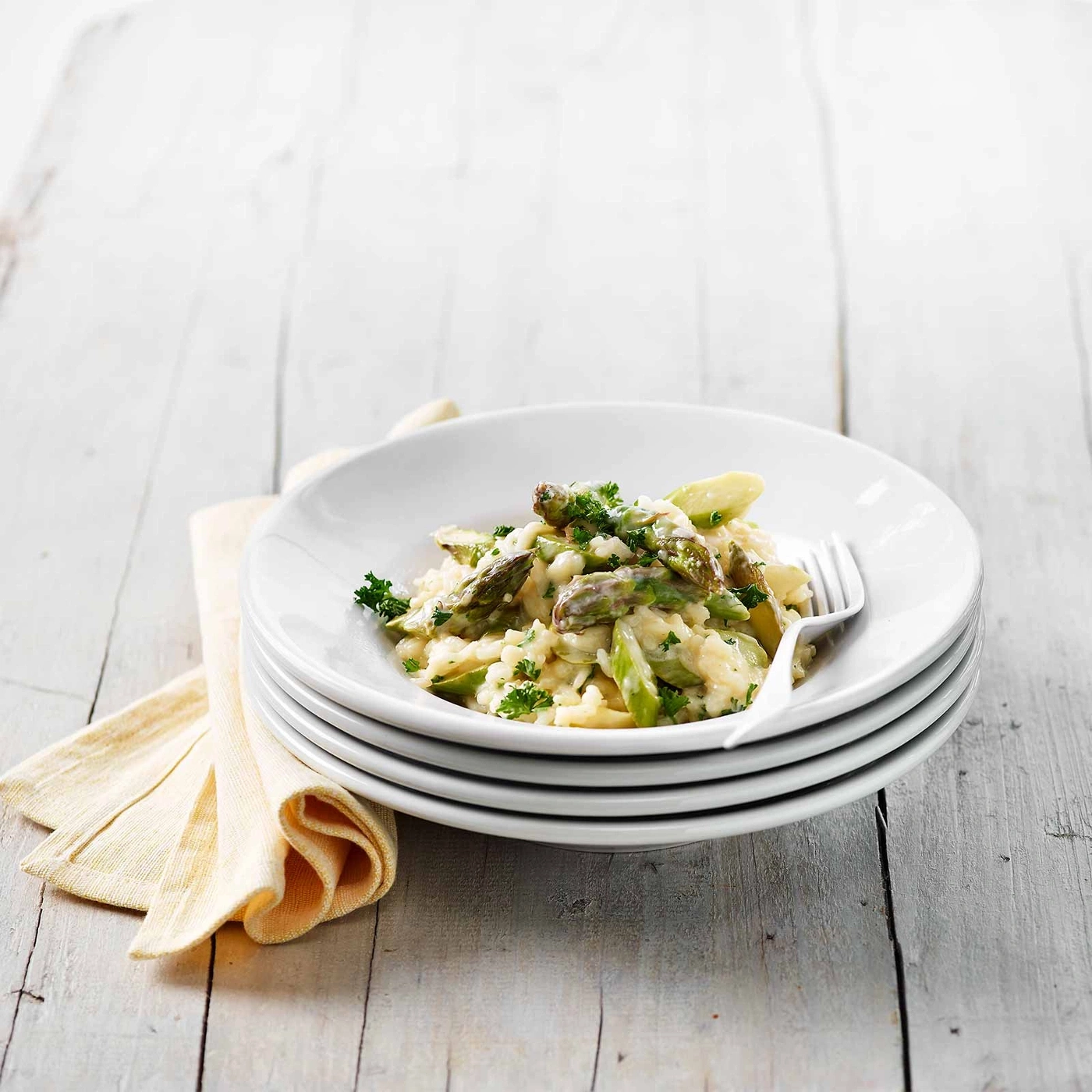 Teller mit Spargel-Risotto, serviert auf einem Holztisch mit gelbem Tuch.