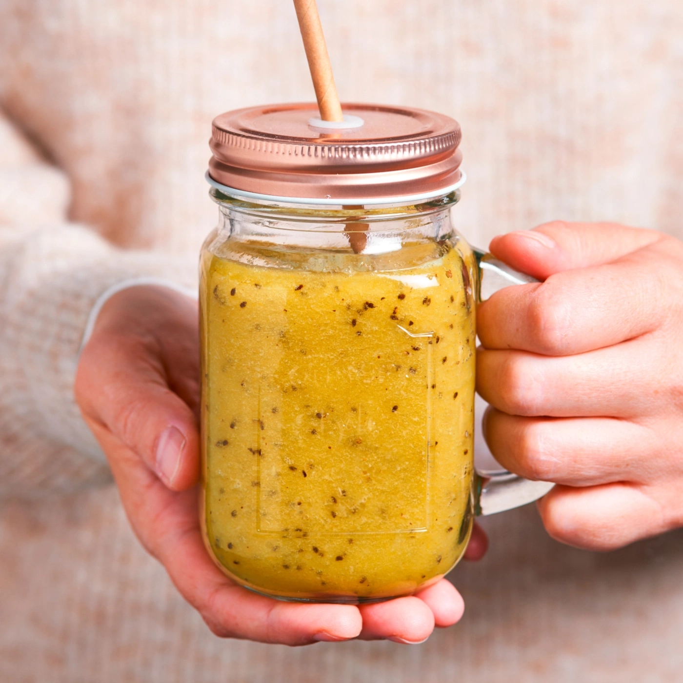 Ein Glas Smoothie mit Strohhalm, gehalten von zwei Händen, Nahaufnahme.