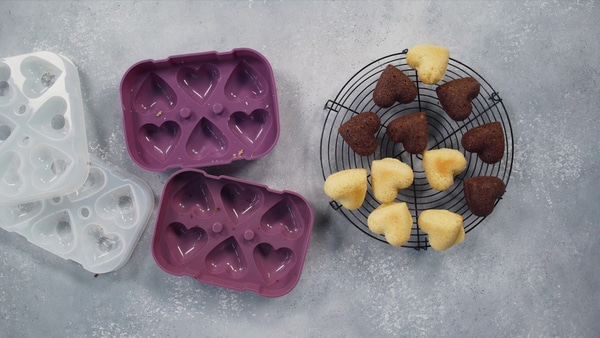 Herzförmige Kuchen auf einem Rost mit Backformen auf grauem Hintergrund.
