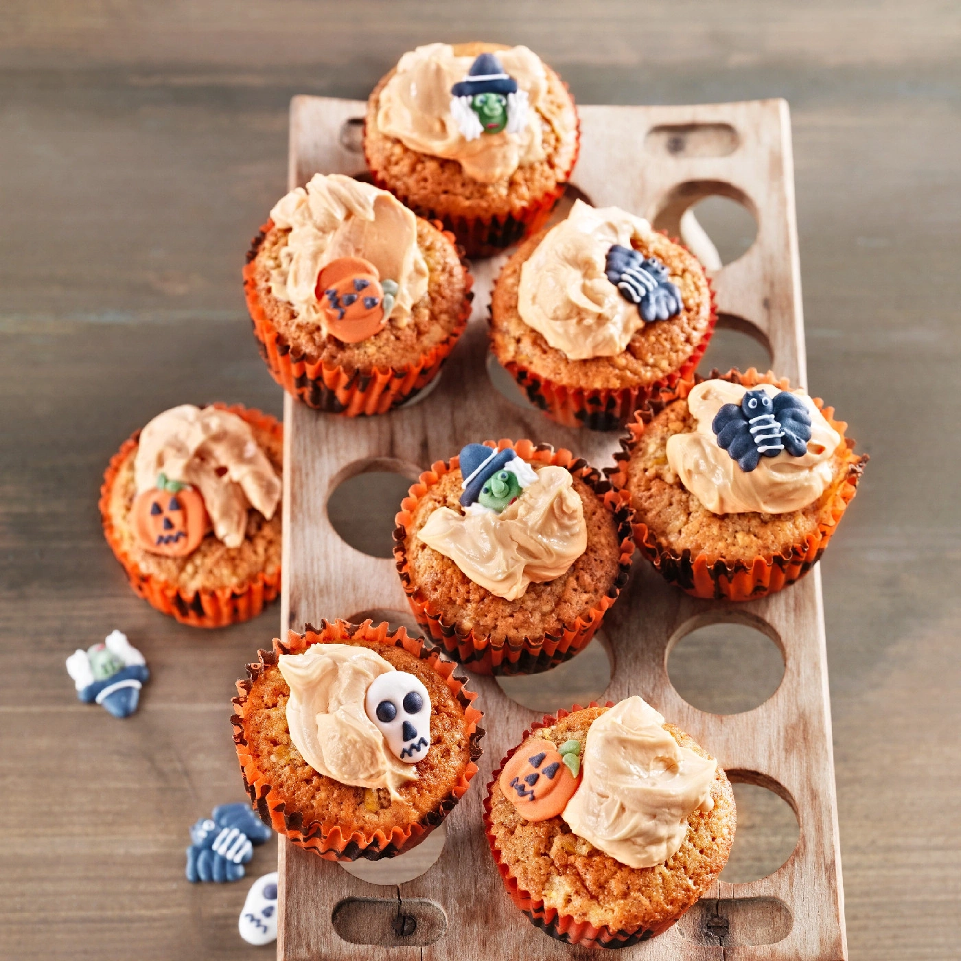 Halloween-Cupcakes mit Dekorationen auf einem Holzbrett, lecker und gruselig.