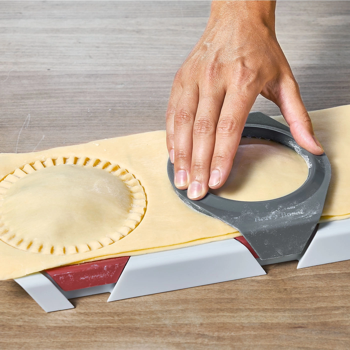 Main coupant la pâte avec un outil pour former des tartes. Gros plan.