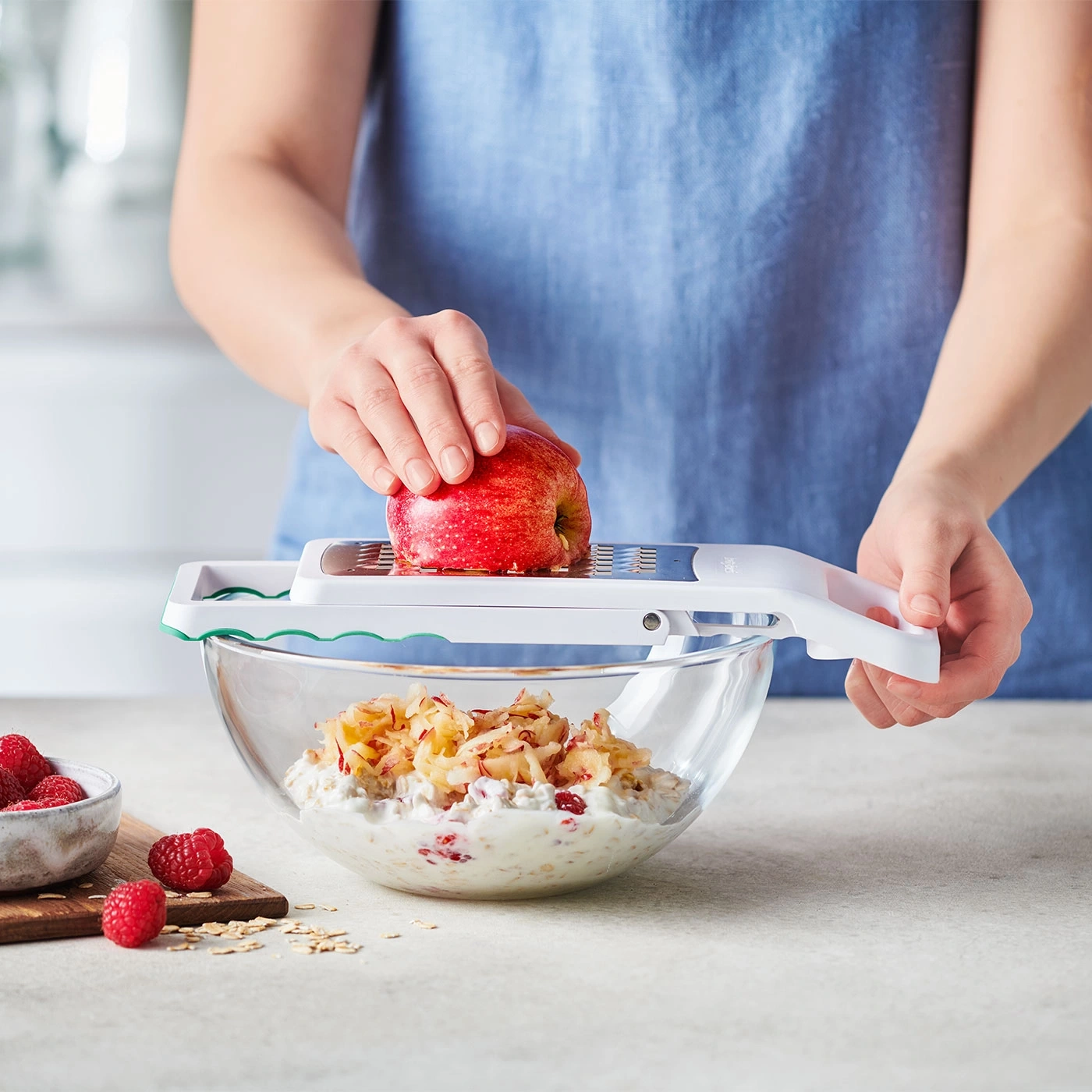 Personne râpe une pomme sur du muesli avec des framboises dans un bol en verre