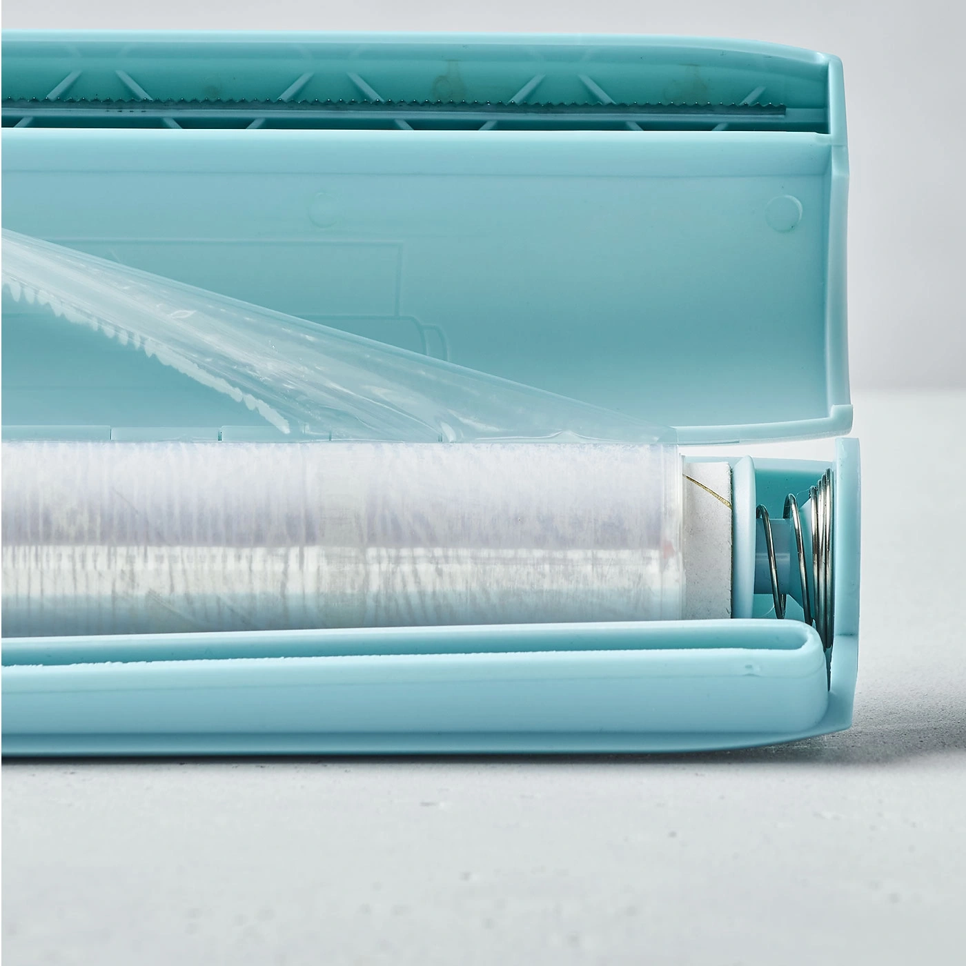 Blauer Plastik-Folienroller mit Folie und Feder, Nahaufnahme, hellgrauer Hintergrund.