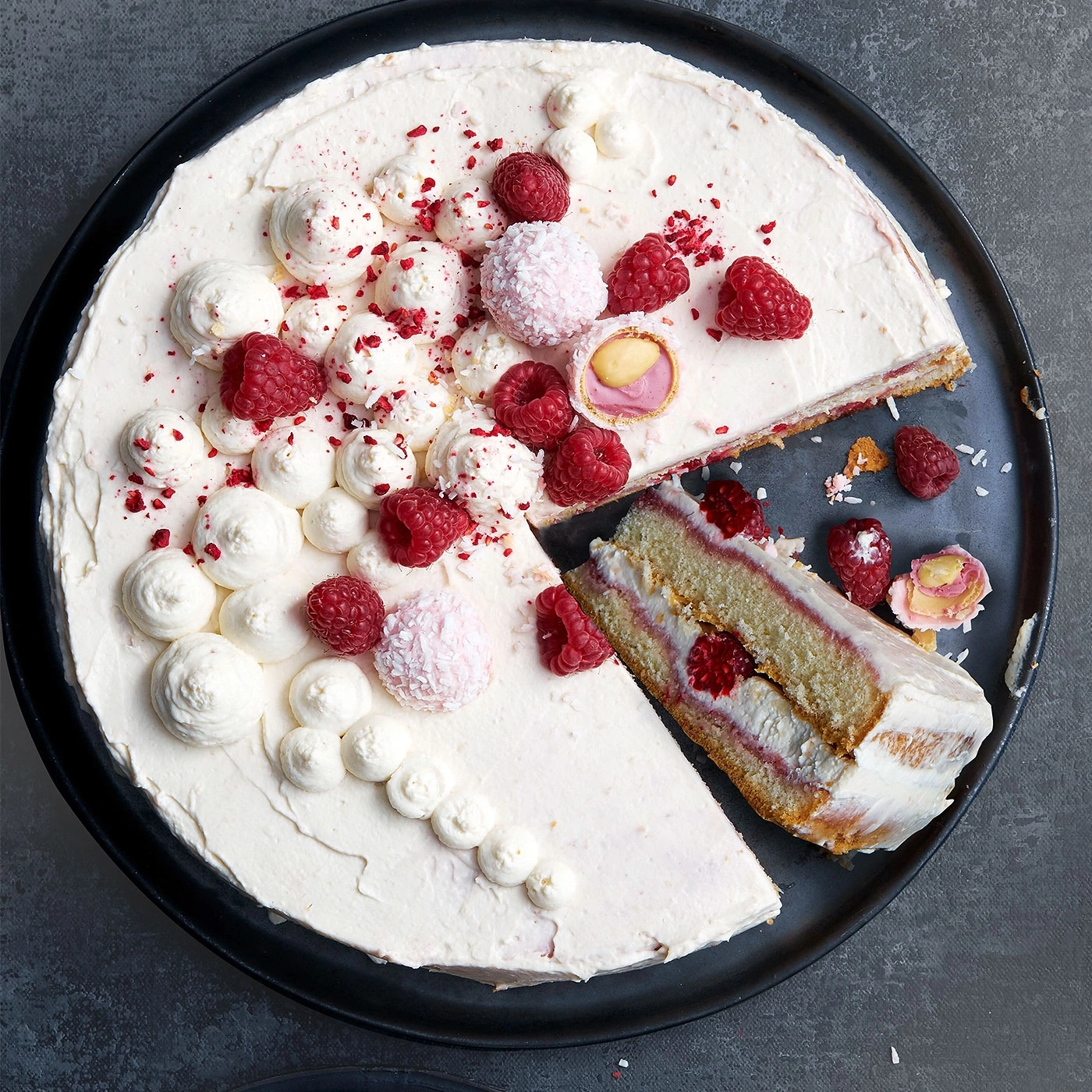 Himbeerkuchen mit Sahne, Beeren und Kokosraspeln auf schwarzem Teller