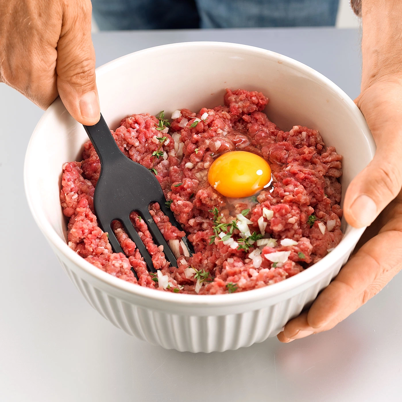 Hände halten Schüssel mit Hackfleisch, Ei und Zwiebeln, mit Gabel verrühren