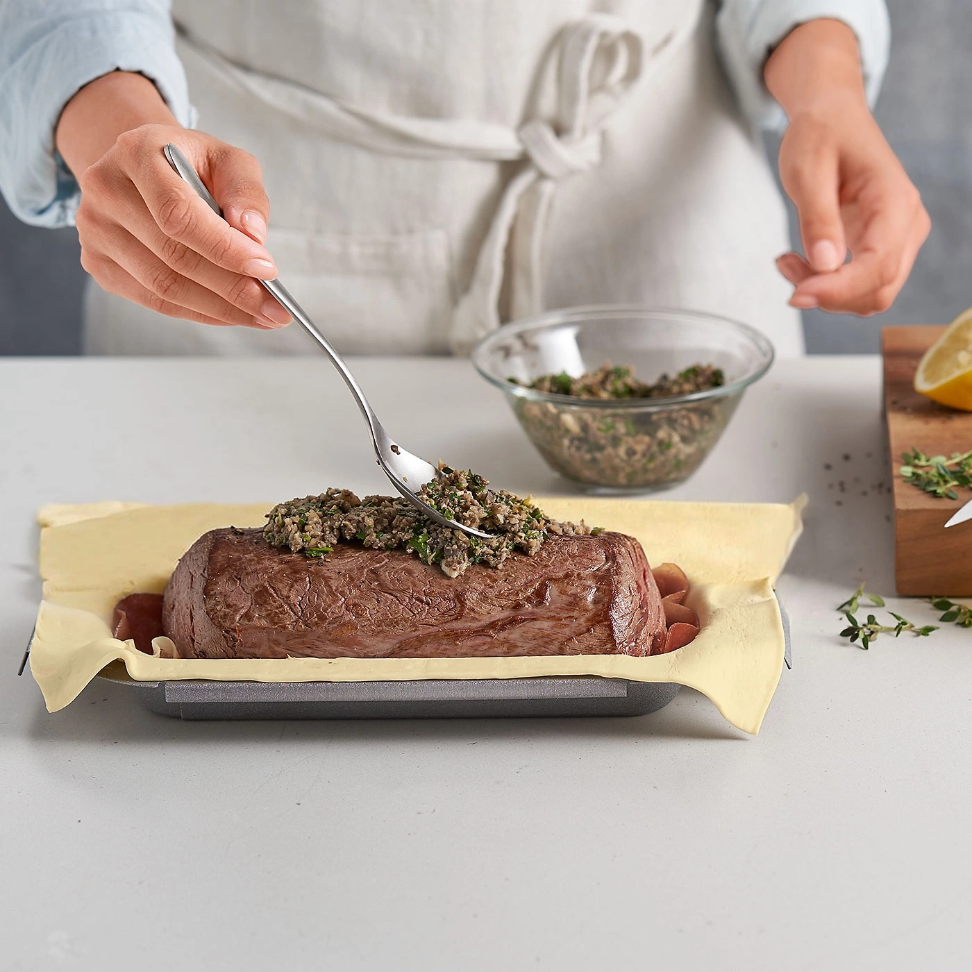 Person bereitet Fleisch zu, das mit einer Gabel belegt wird, in einer Backform.
