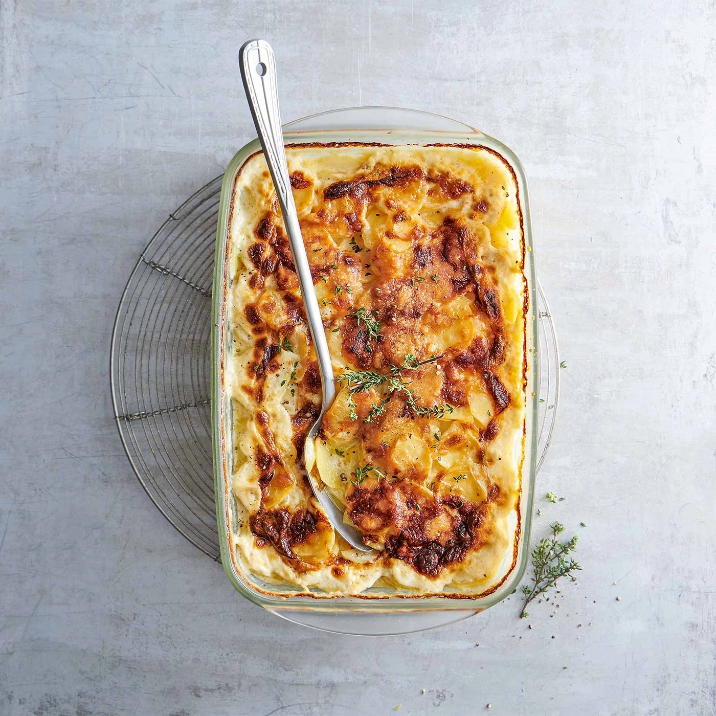 Auflauf mit Kartoffeln und Käse, serviert mit einem Löffel und Kräutern.