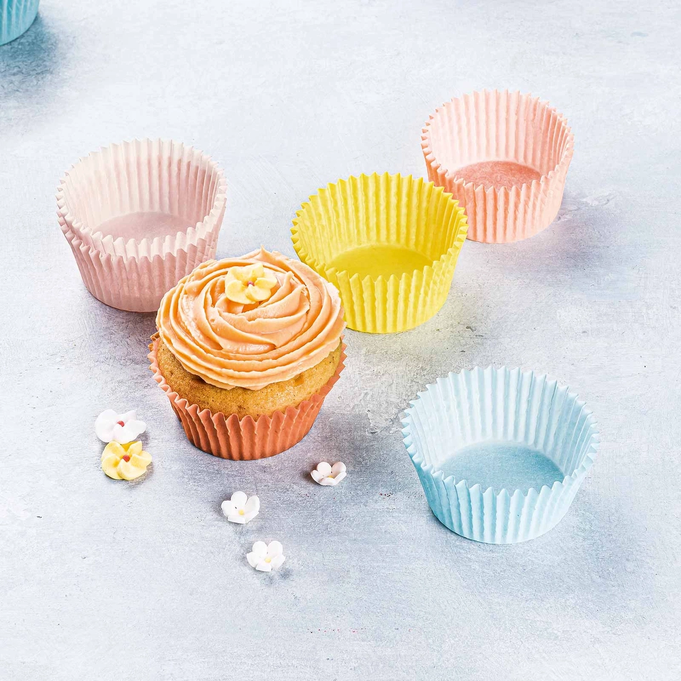 Ein Cupcake mit Blumen und Cupcake-Formen in verschiedenen Farben auf grauem Hintergrund.