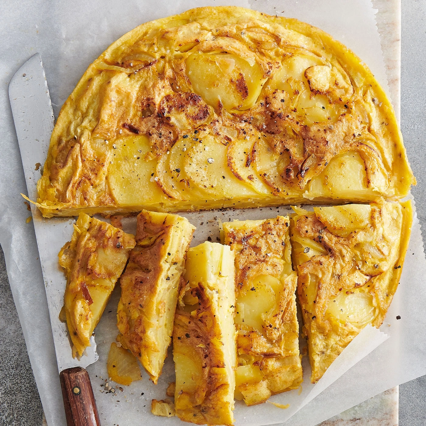 Spanische Tortilla, geschnitten, auf Backpapier, mit Messer, Nahaufnahme, Essen