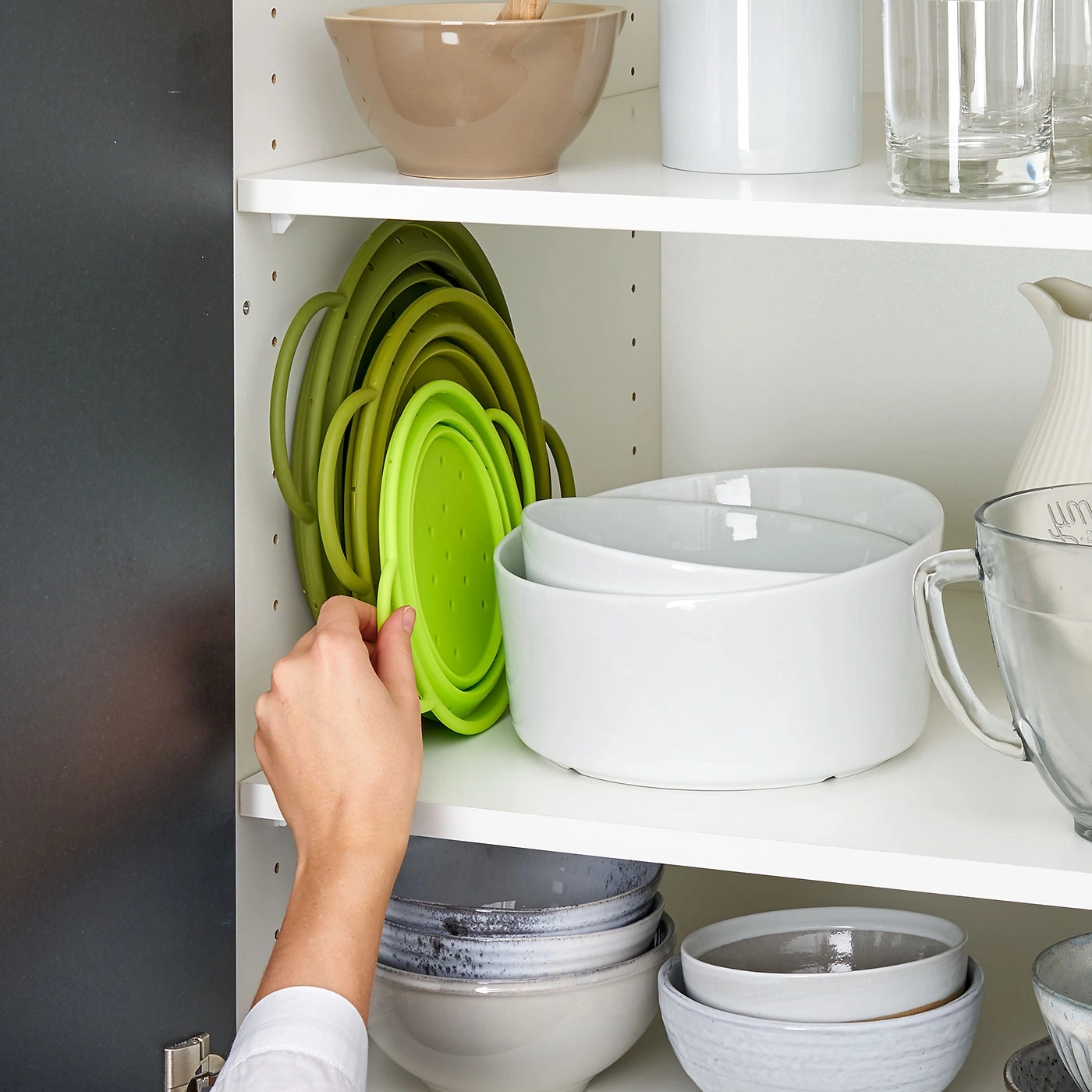 Person, die einen grünen, zusammenklappbaren Sieb aus einem Schrank nimmt.