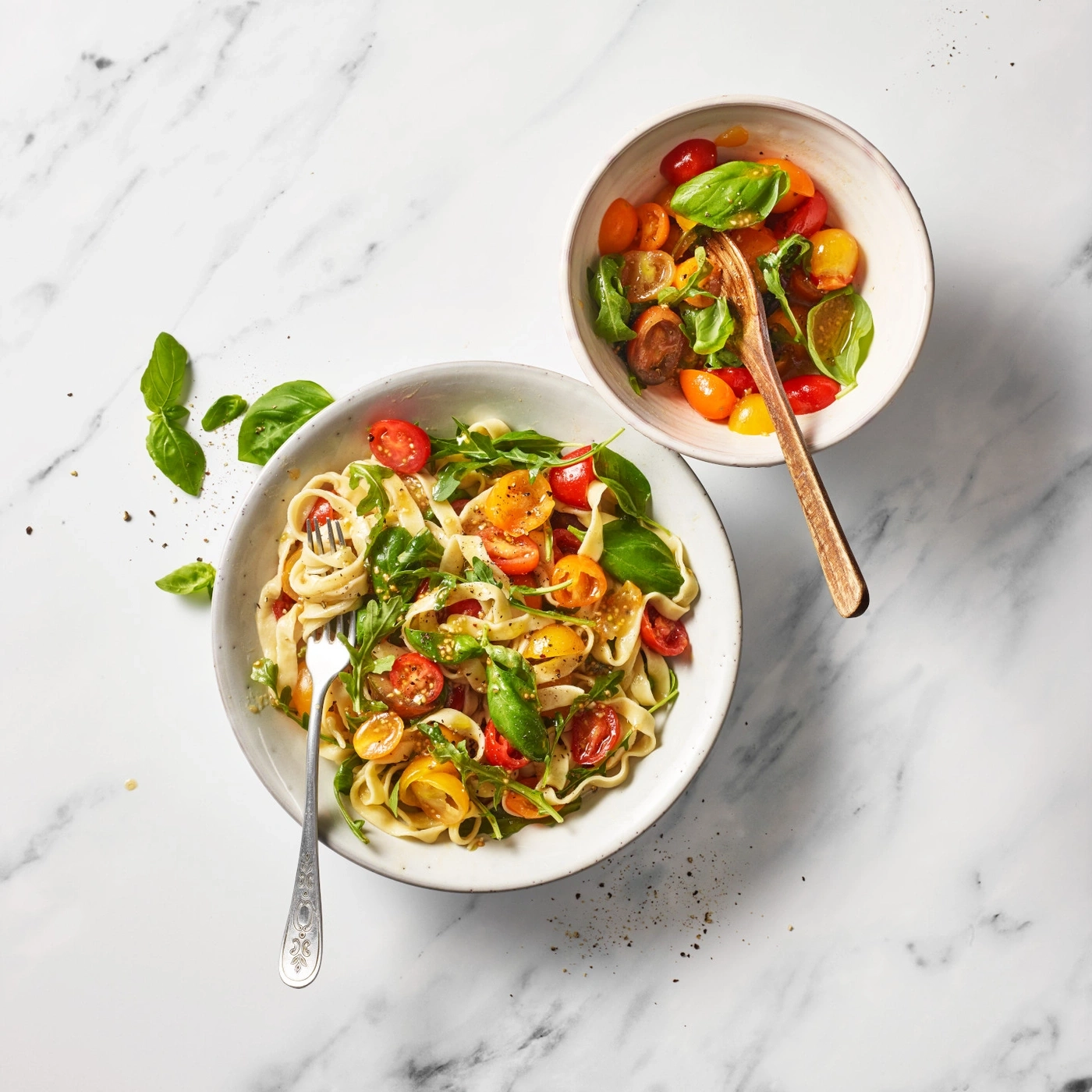 Pasta mit Tomaten und Basilikum in Schalen auf Marmortischplatte