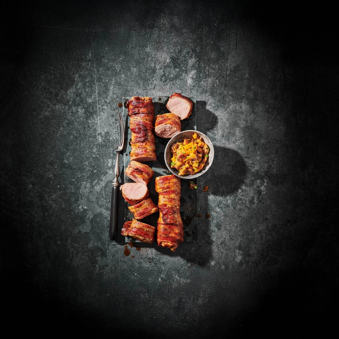 Viande enveloppée de bacon avec accompagnement sur fond sombre
