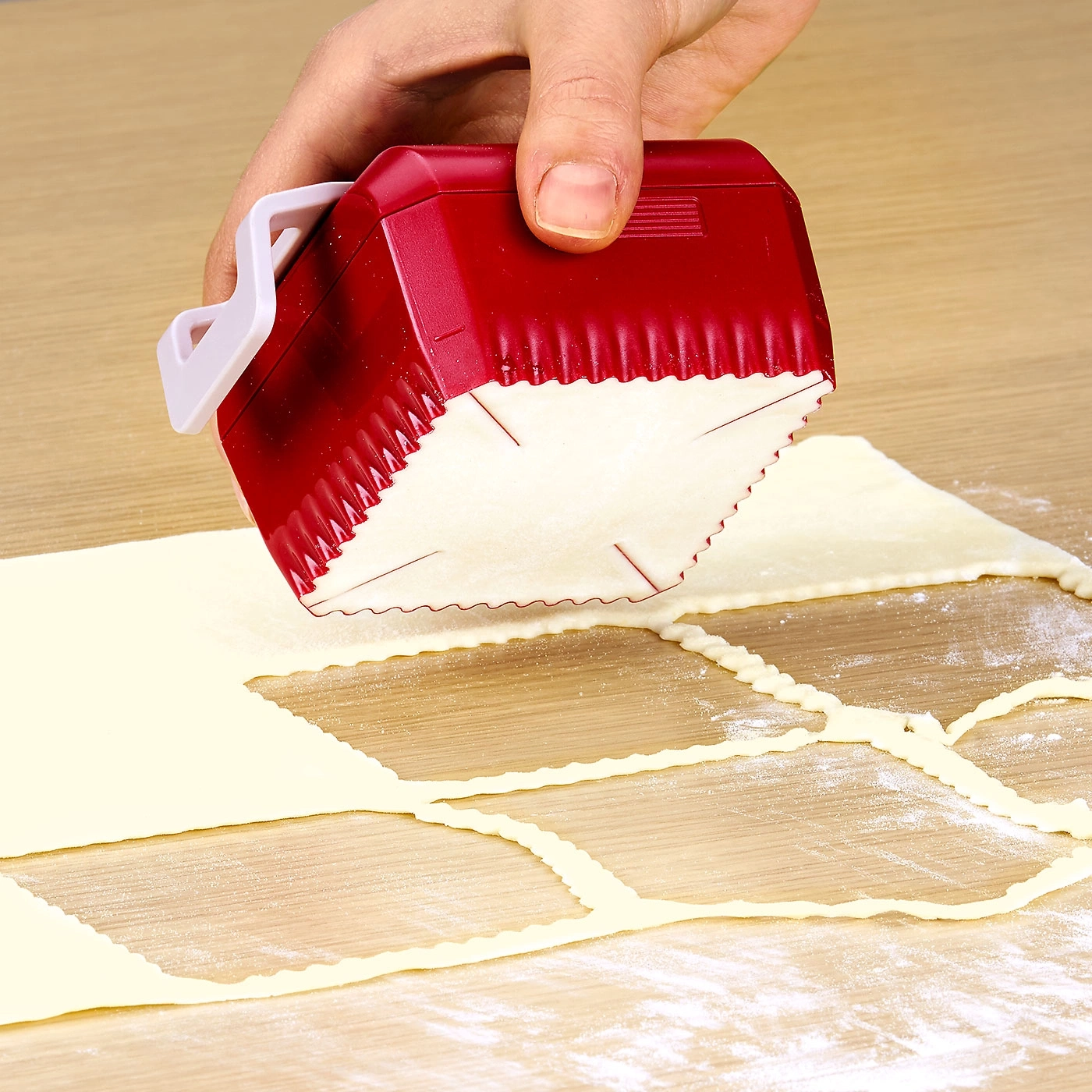 Hand schneidet Teig mit rotem Werkzeug auf Holzoberfläche.