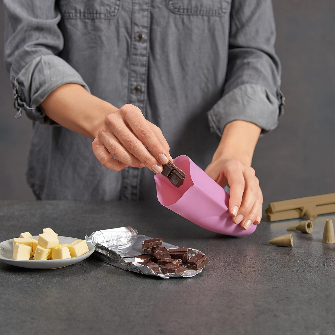 Person legt Schokoladenstücke in einen rosa Beutel. Butter und Spritztüllen liegen bereit.