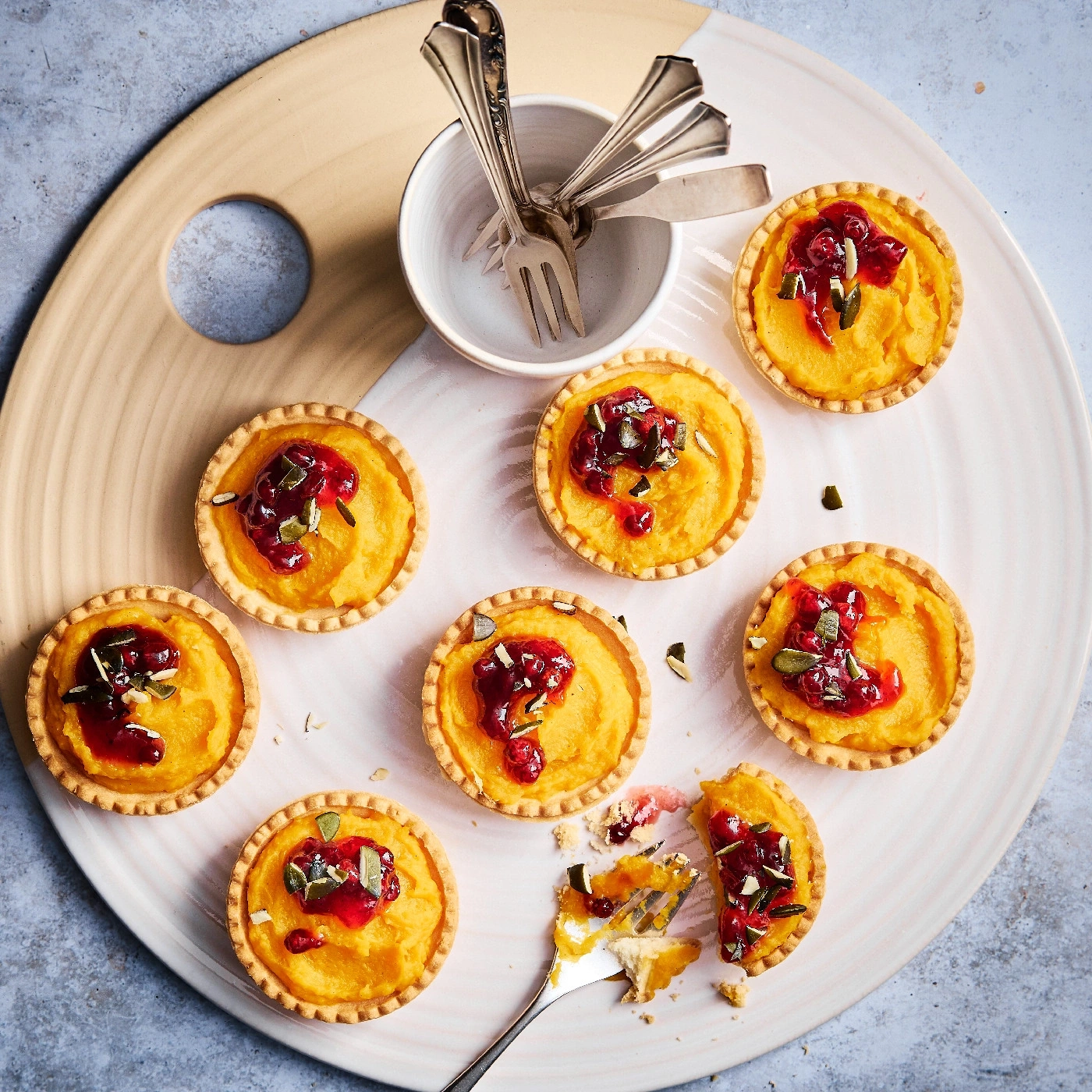 Kürbistörtchen mit Cranberry-Topping auf einem Teller mit Gabeln und einem Brett.