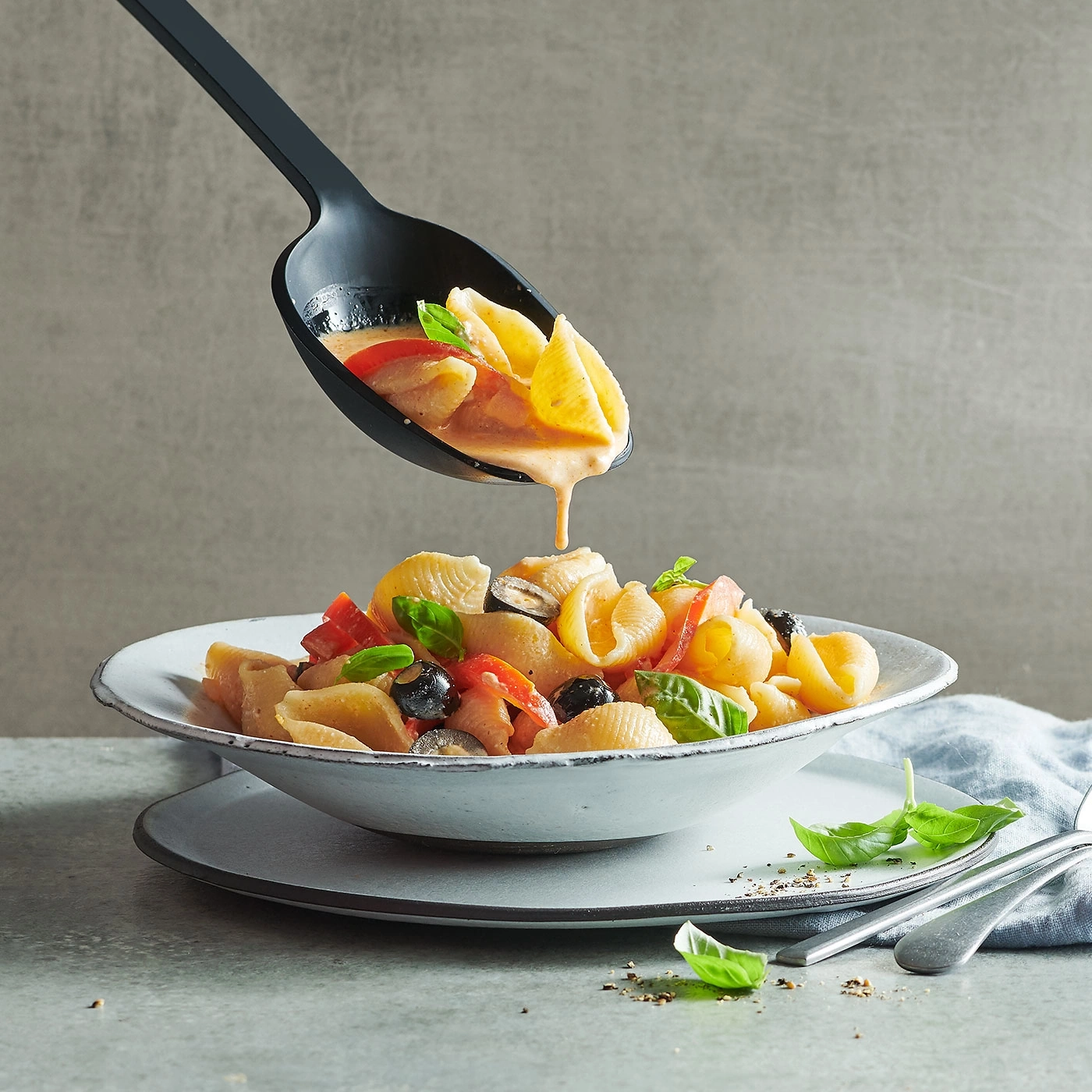 Pasta-Gericht mit Oliven, Tomaten und Basilikum, serviert mit Soße in einer Schüssel