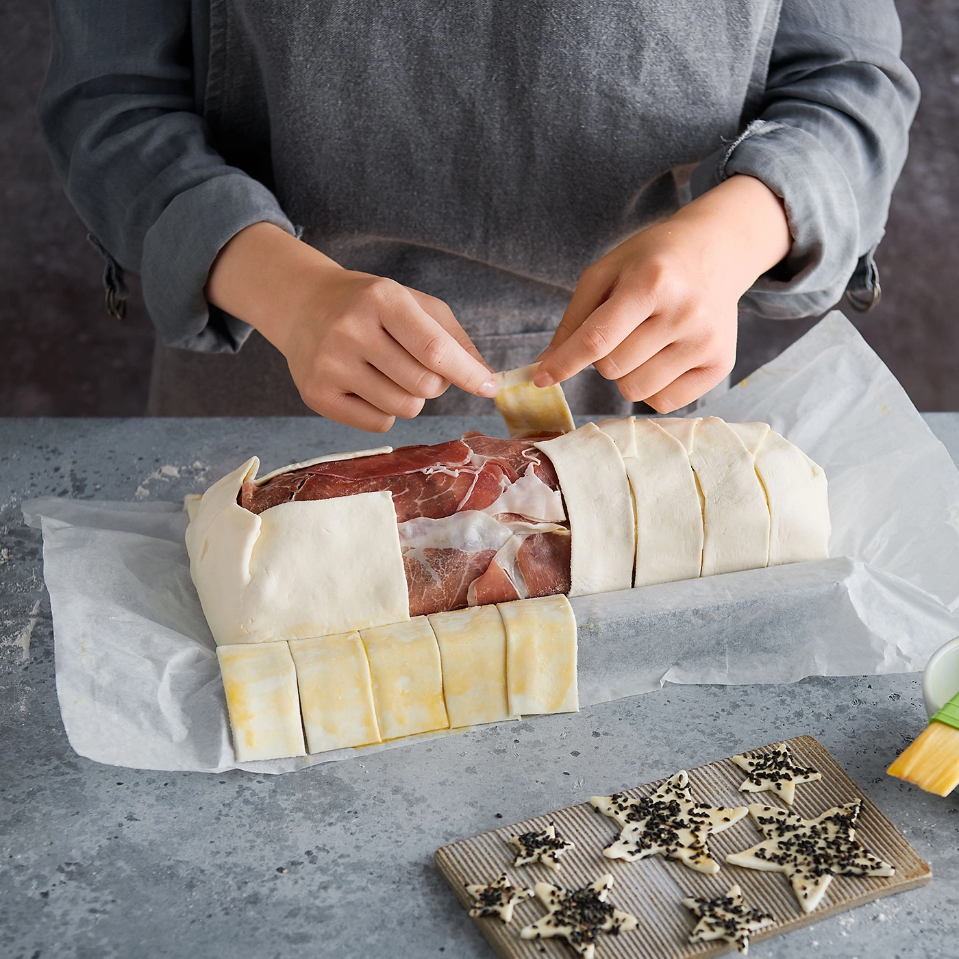 Person bereitet Fleisch zu, das in Teig gewickelt ist, auf einem Tisch.