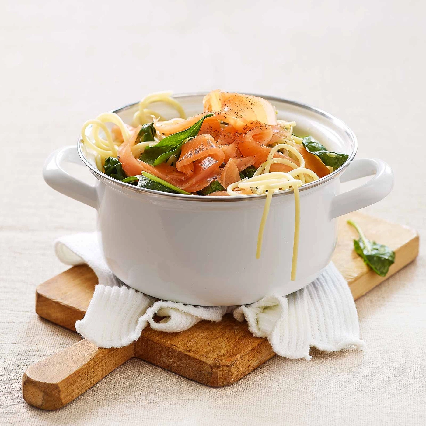 Pasta mit Lachs und Spinat in einem Topf auf einem Holzbrett