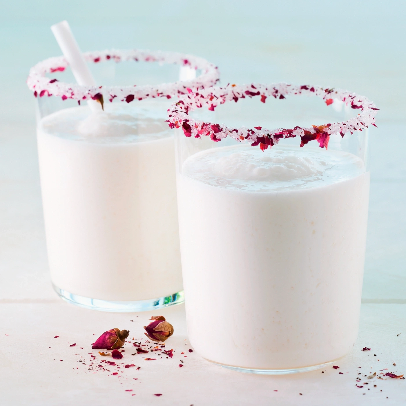 Zwei Gläser mit rosa Getränk, dekoriert mit Rosenblättern und Zucker.