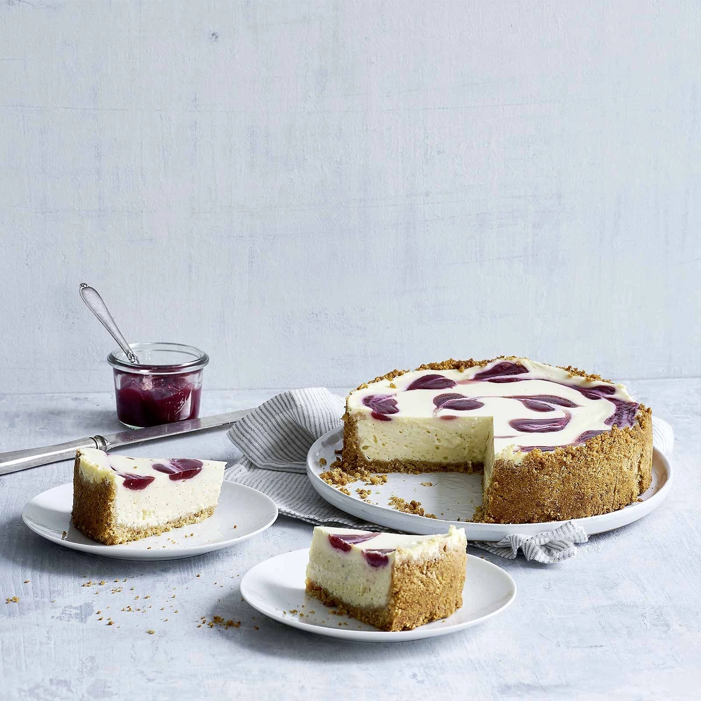 Käsekuchen mit Kirschen, serviert auf Tellern, mit Marmelade und Messer.